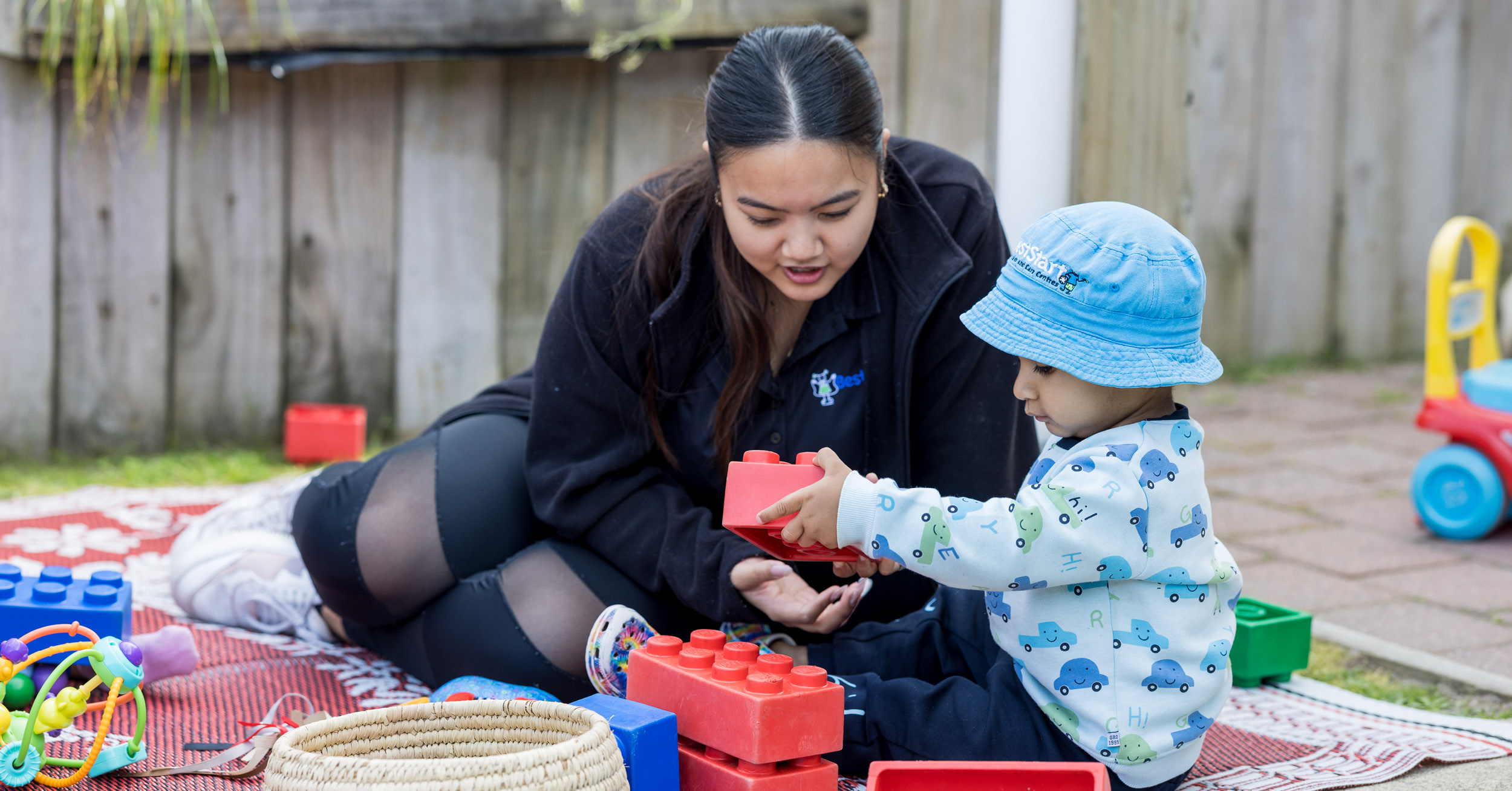 1727728508Teacher and baby on mat and blocks Sept2024.jpg