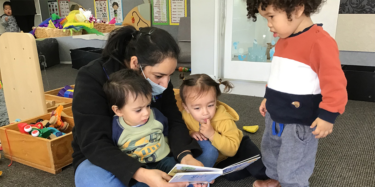 3 kids reading book with teacher 
